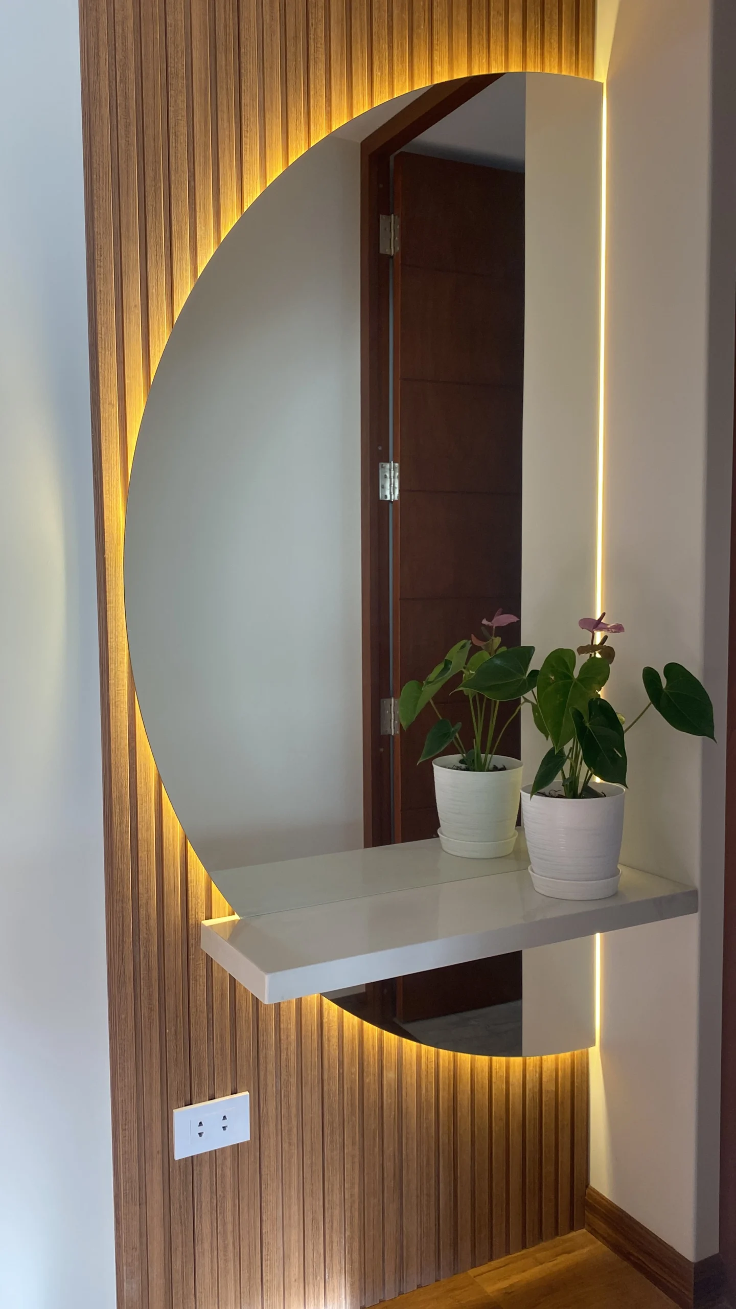 Recibidor moderno con panel decorativo de madera, espejo circular e iluminación indirecta en Arequipa